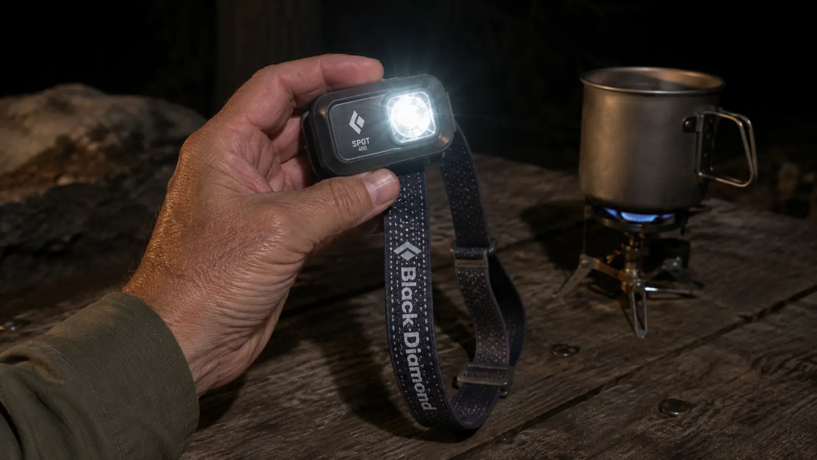 Black Diamond Spot 400 headlamp held in a hand over a campsite picnic table with cooking gear